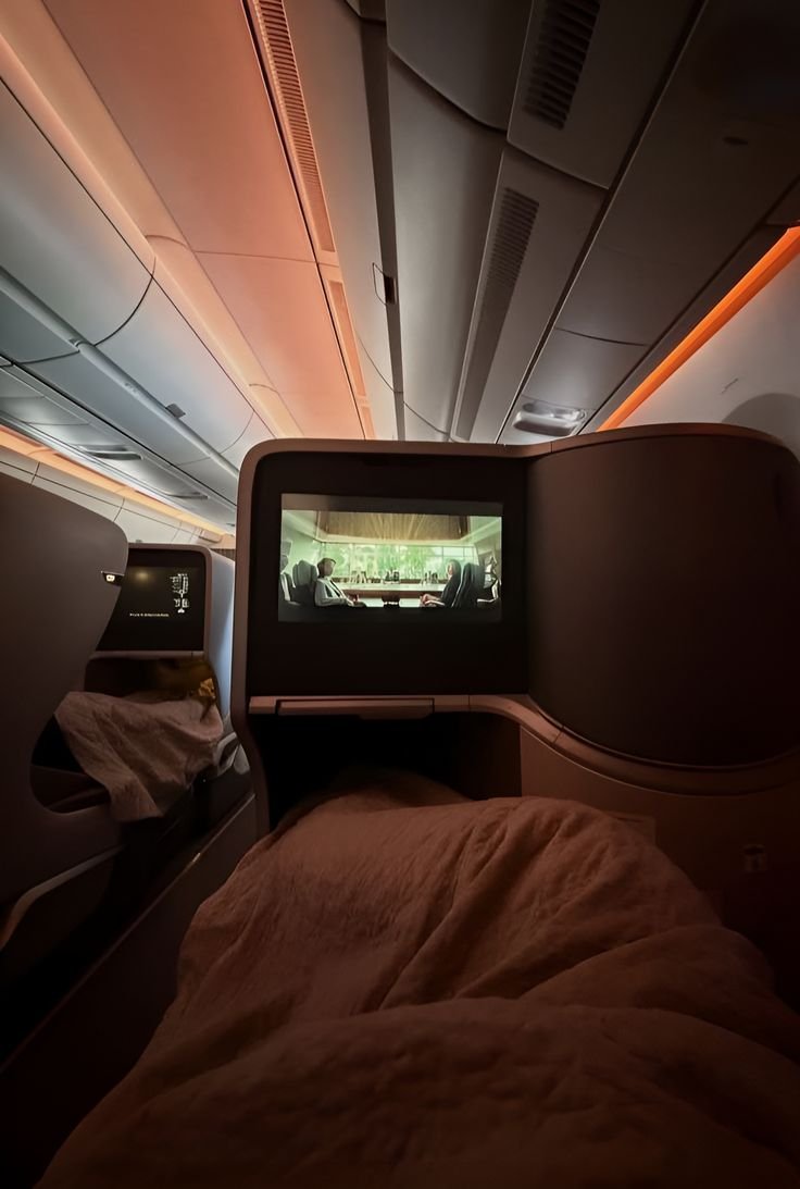 Lie flat bed facing a large entertainment screen under warm cabin light